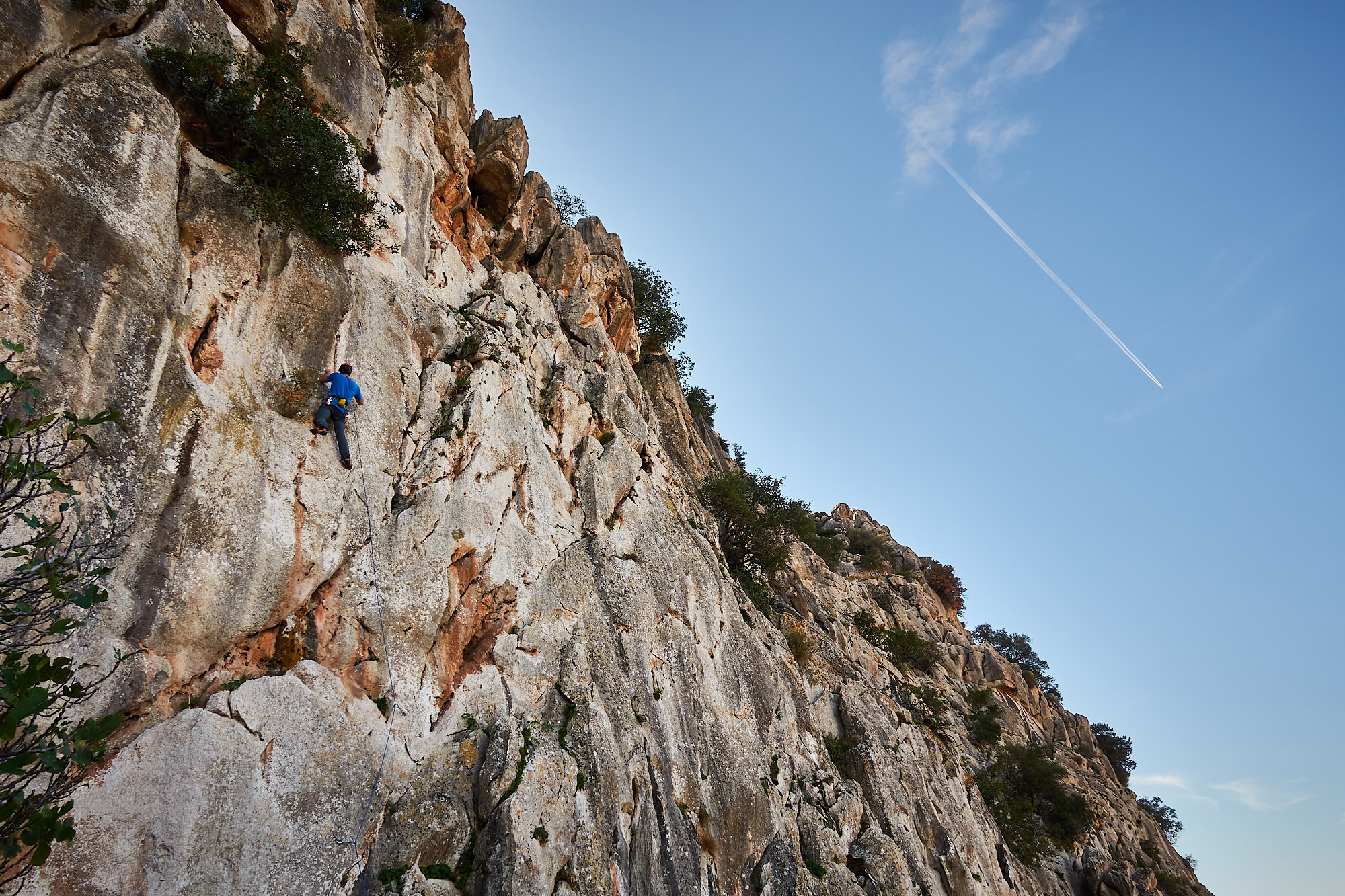 A climber sport climbing on a limestone cliff in southern Spain with blue sky above