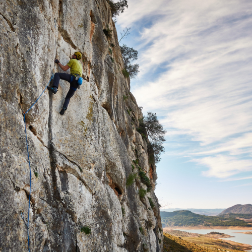A climber sport climbing on a limestone crack in southern Spain with hills and a lake in the background