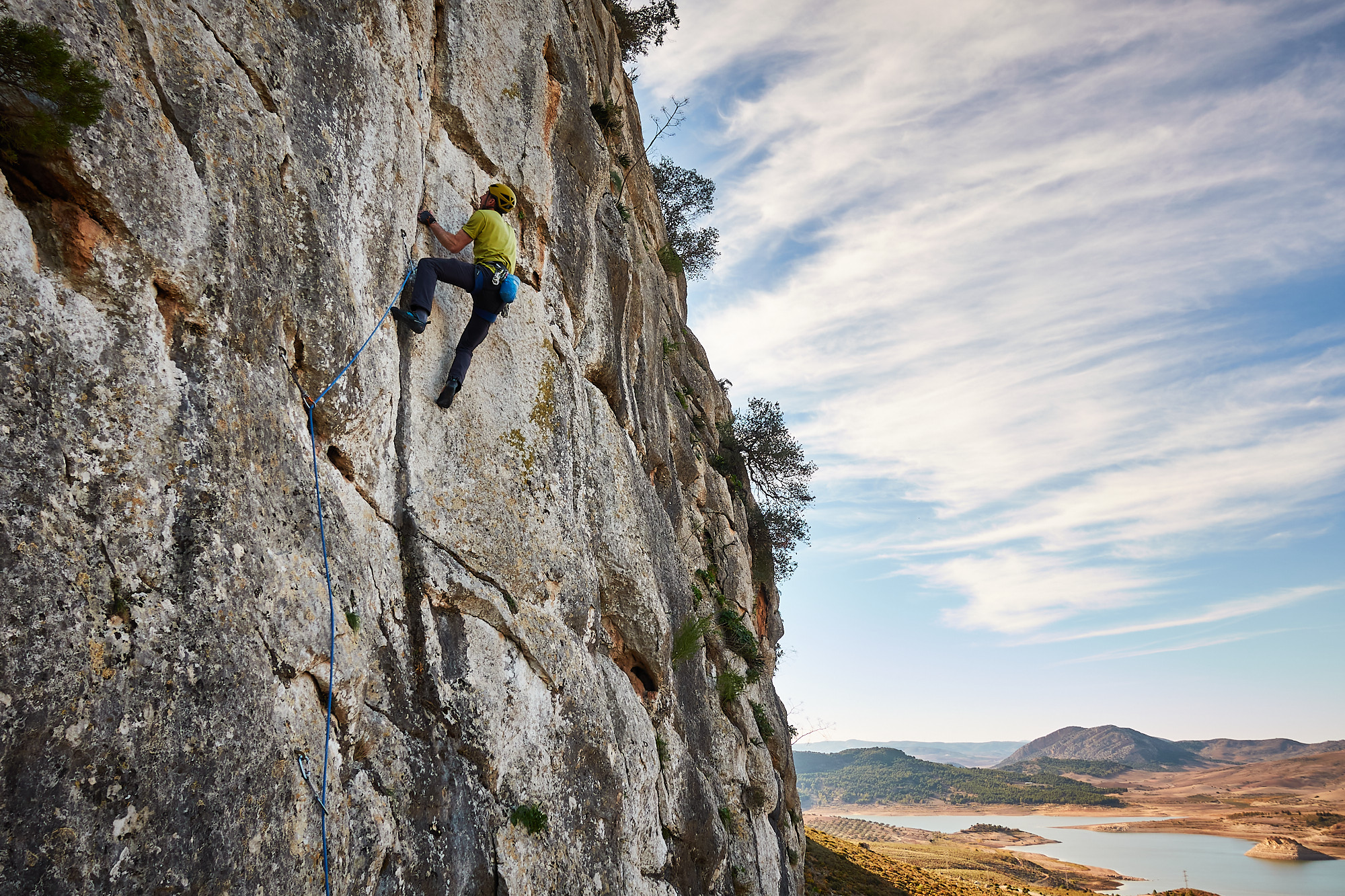 A climber sport climbing on a limestone crack in southern Spain with hills and a lake in the background
