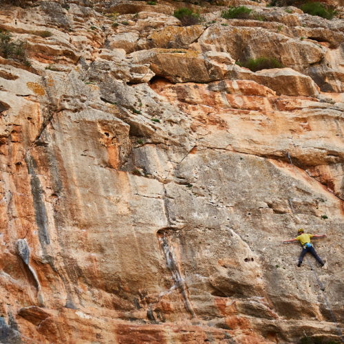 A climber sport climbing on a grey and orange limestone cliff in southern Spain with no hands on the rock