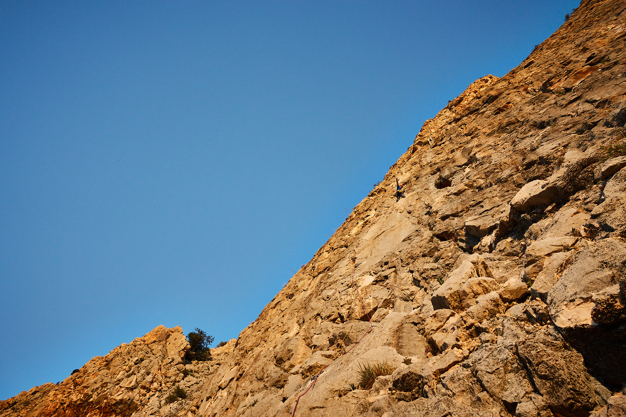 A climber sport climbing on the first pitch of a route called Amptrax on a limestone cliff in southern Spain with blue sky above