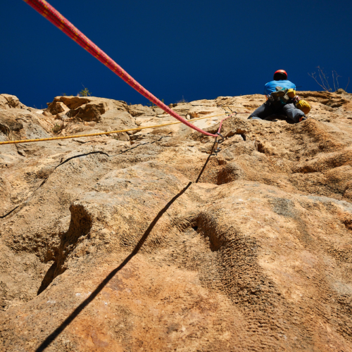 A climber sport climbing on the third pitch of a route called Amptrax on a limestone cliff in southern Spain with blue sky above