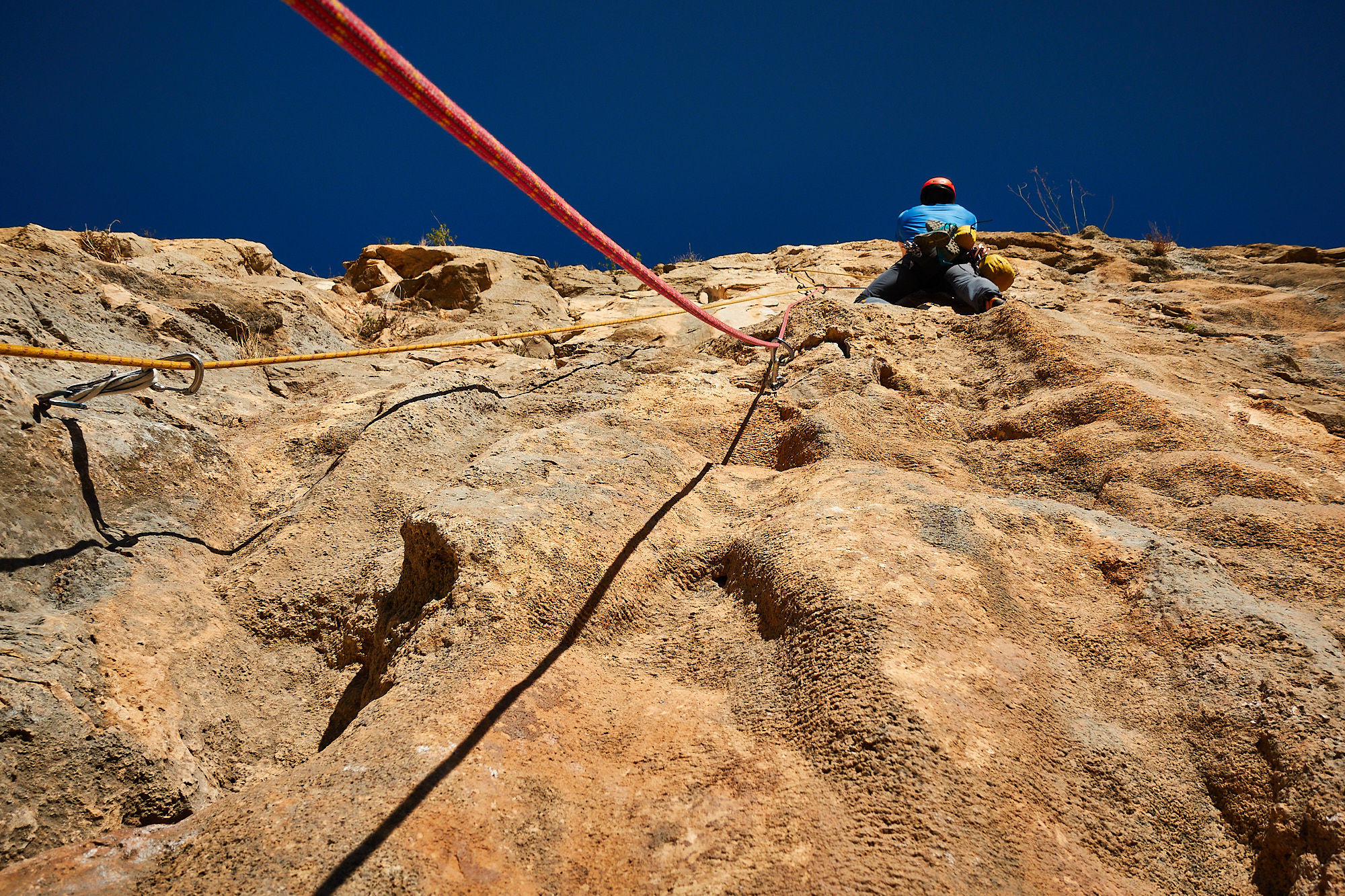 A climber sport climbing on the third pitch of a route called Amptrax on a limestone cliff in southern Spain with blue sky above