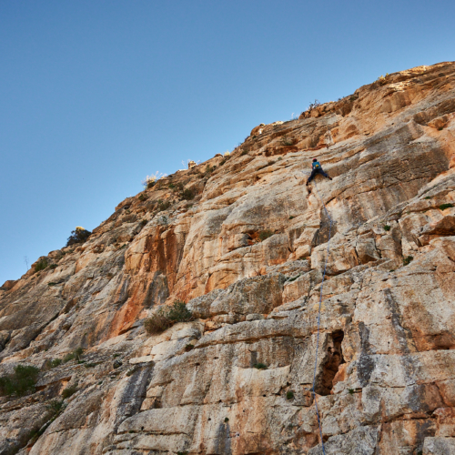 A climber sport climbing on a grey and orange limestone cliff in southern Spain with blue sky above