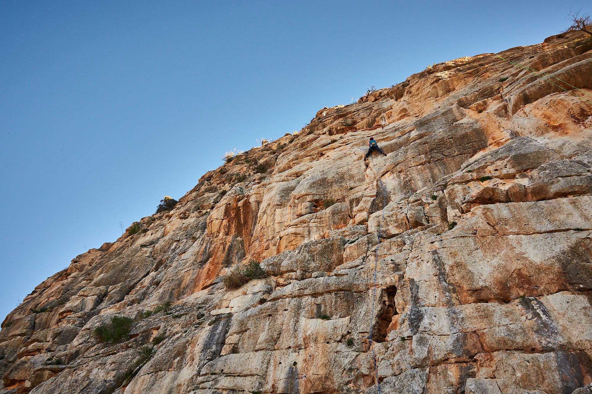 A climber sport climbing on a grey and orange limestone cliff in southern Spain with blue sky above
