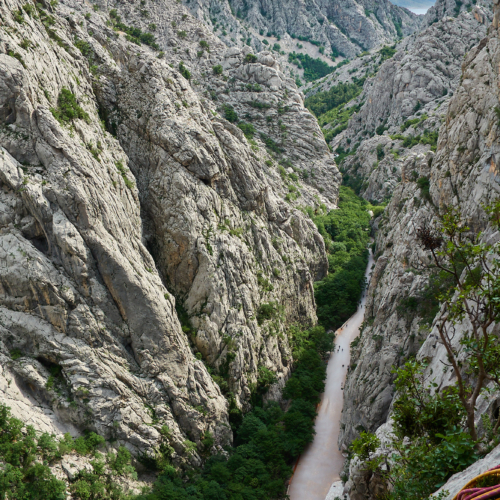 A view of some large limestone cliffs with trees below and blue sky above in the Paklenica gorge in Croatia