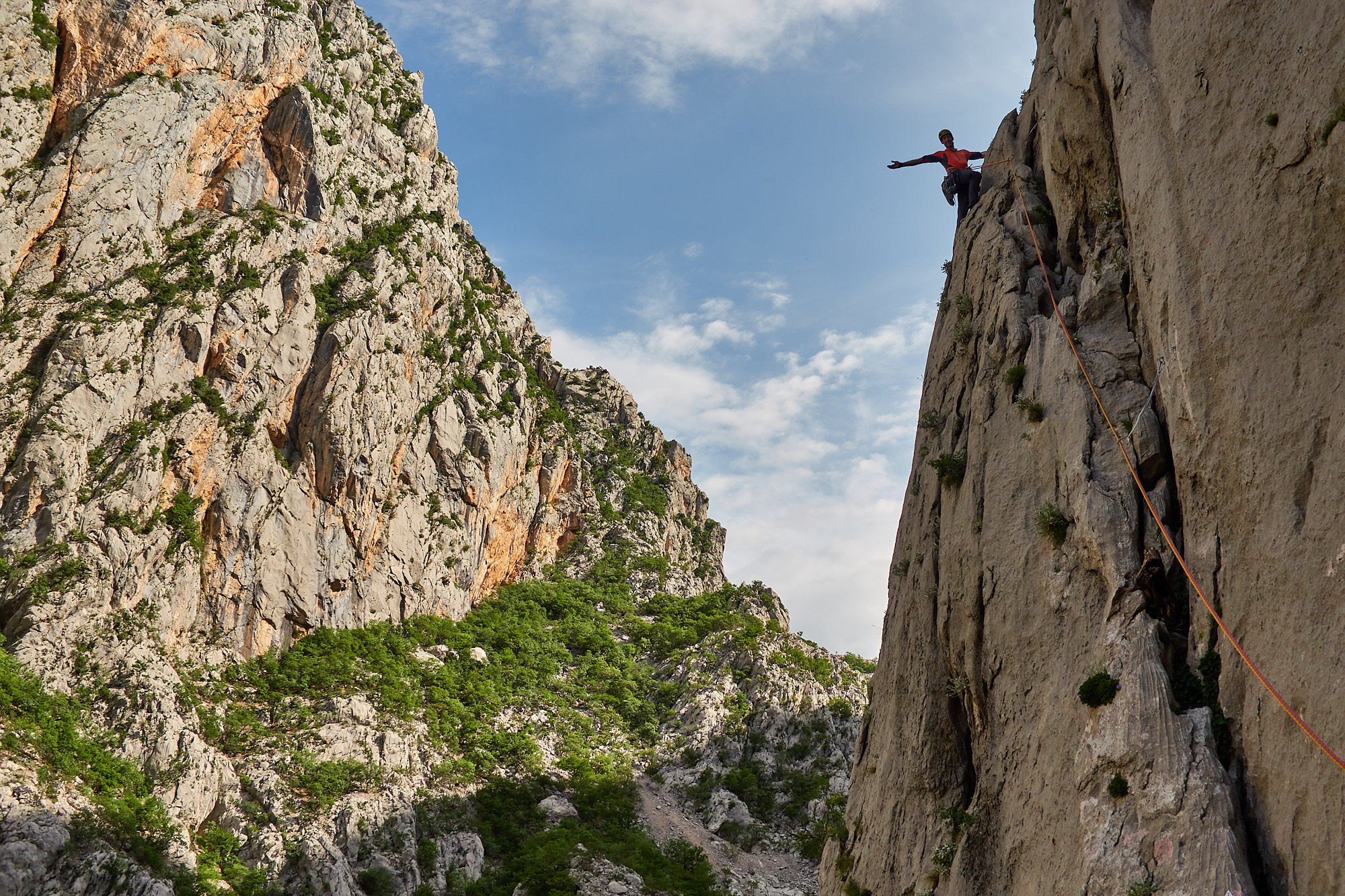 A climber on a limestone sport climb with trees and blue sky behind in the Paklenica gorge in Croatia