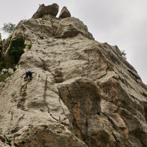 A climber on a limestone sport climb with trees and grey sky behind in the Paklenica gorge in Croatia