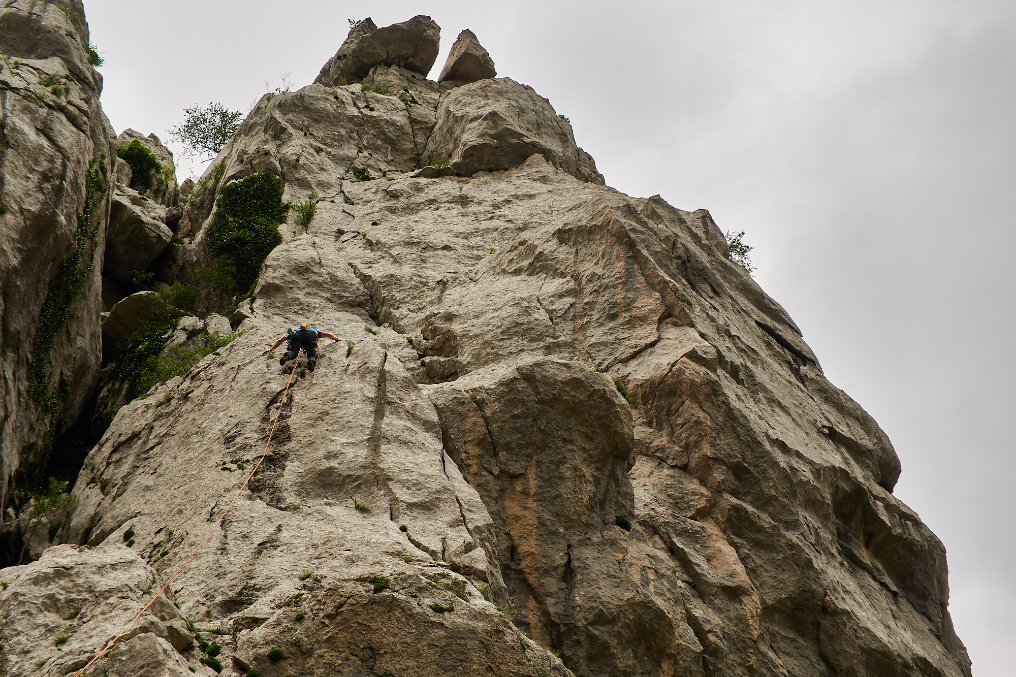 A climber on a limestone sport climb with trees and grey sky behind in the Paklenica gorge in Croatia