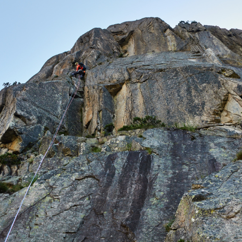 A climber in orange climbing a steep granite corner system on a route called Fairhands Line in the Grimsel Pass