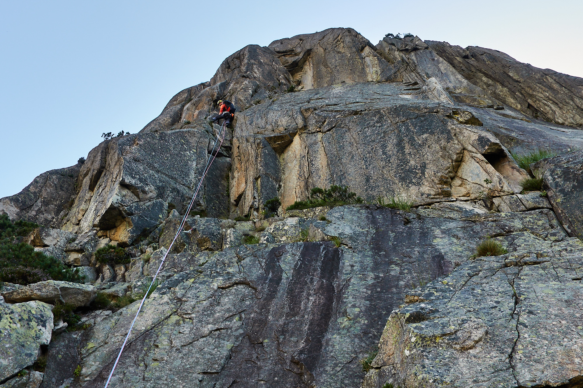 A climber in orange climbing a steep granite corner system on a route called Fairhands Line in the Grimsel Pass