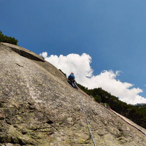 A climber in blue climbing a steep granite slab on a route called Fairhands Line in the Grimsel Pass