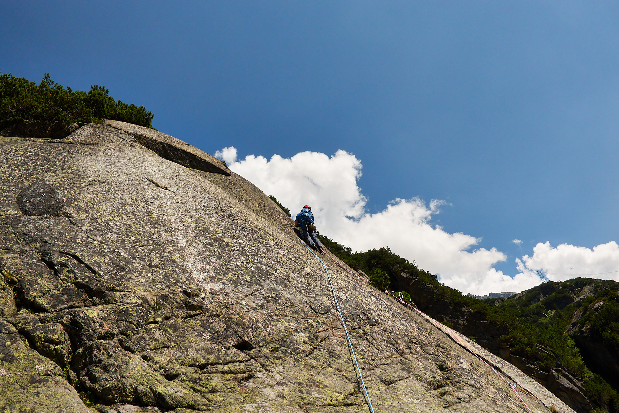 A climber in blue climbing a steep granite slab on a route called Fairhands Line in the Grimsel Pass