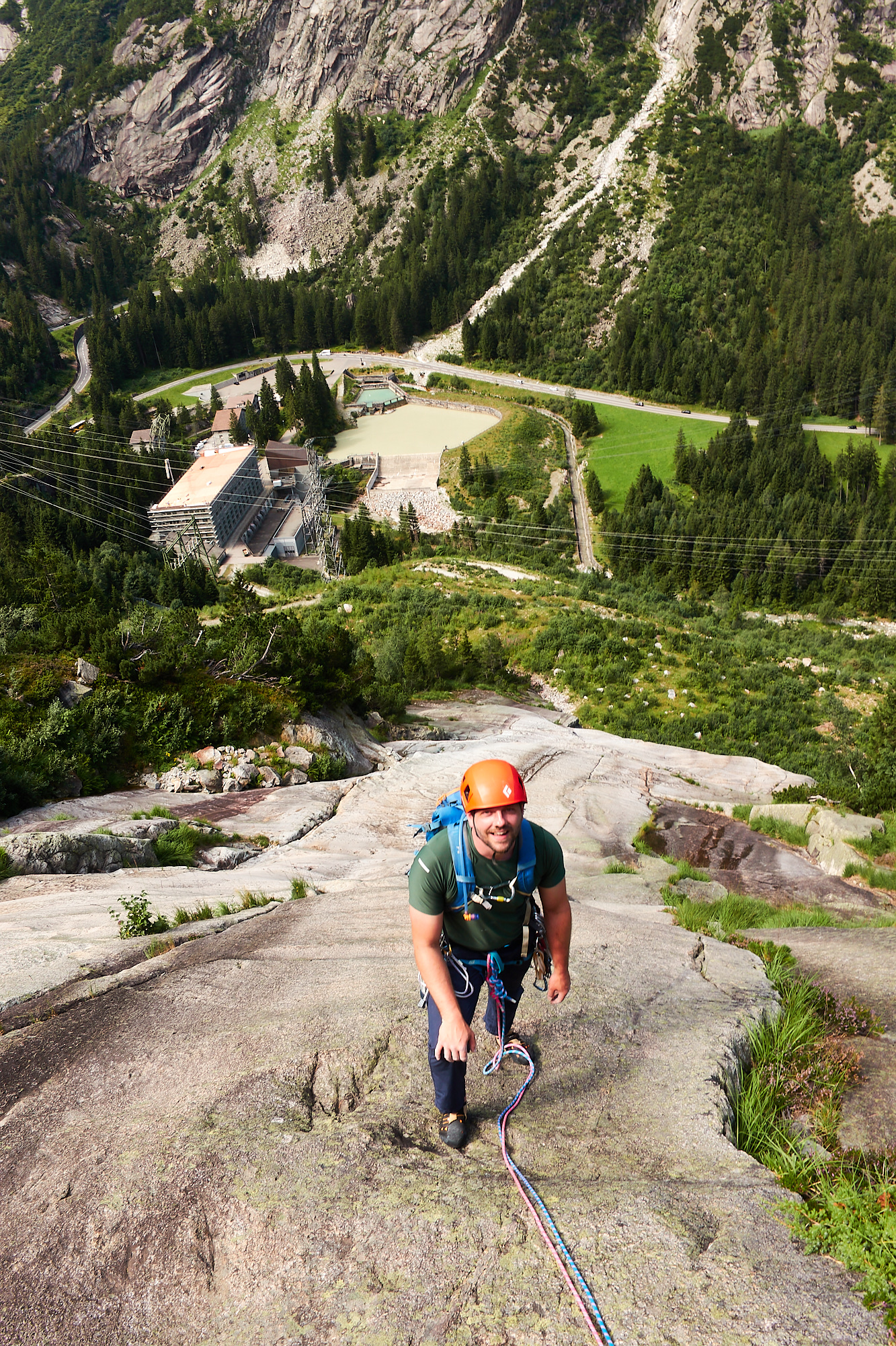 Looking down at a climber at the top of a sweep of clean granite slabs with the valley below