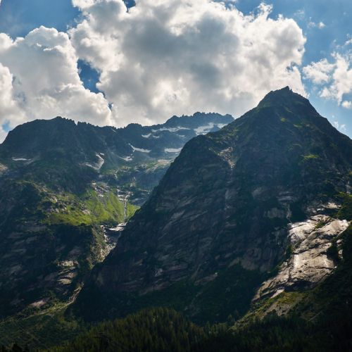 A dramatic view of mountains in shadow with the sun shining on granite slabs and thunder clouds building above