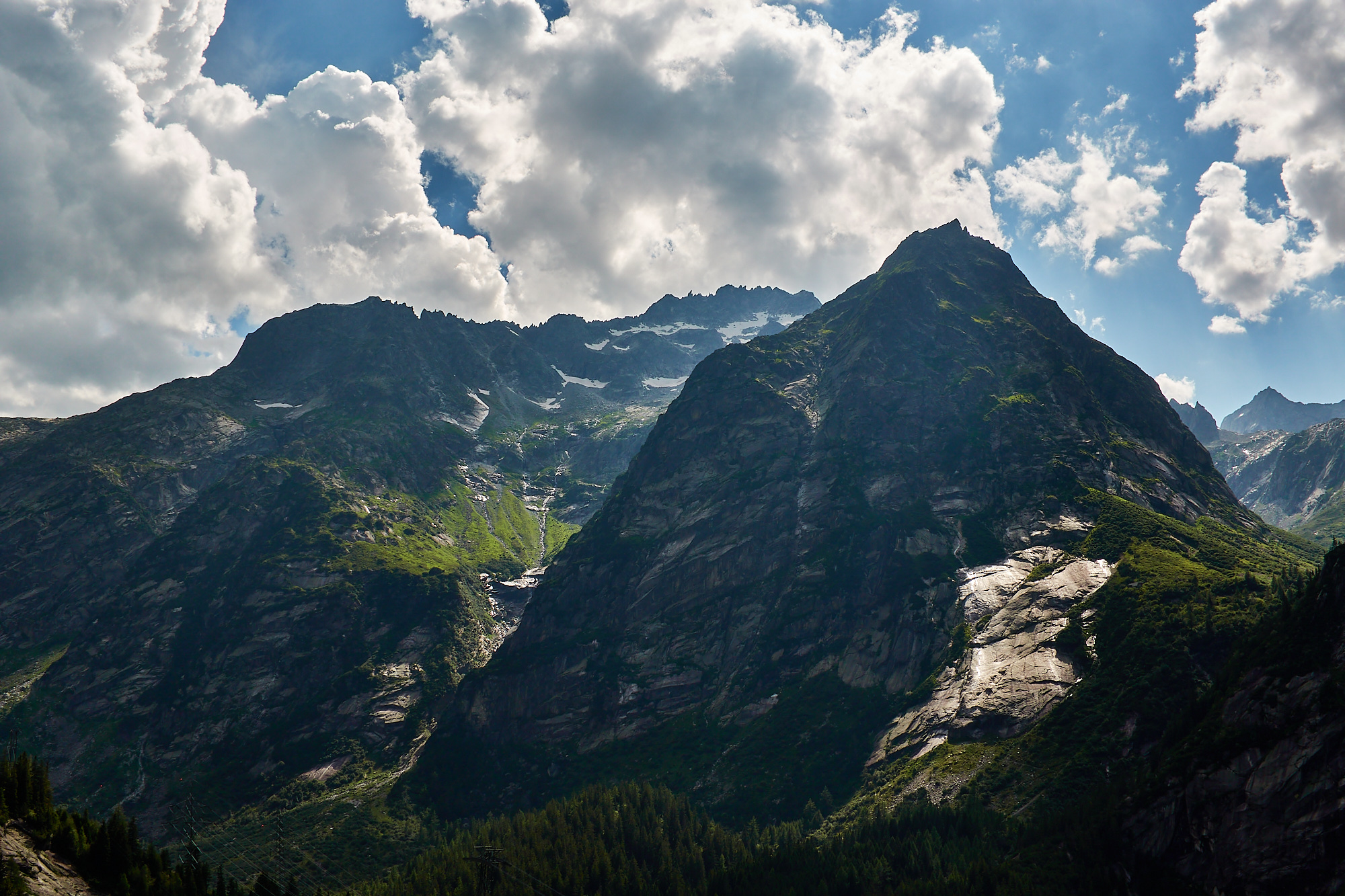 A dramatic view of mountains in shadow with the sun shining on granite slabs and thunder clouds building above