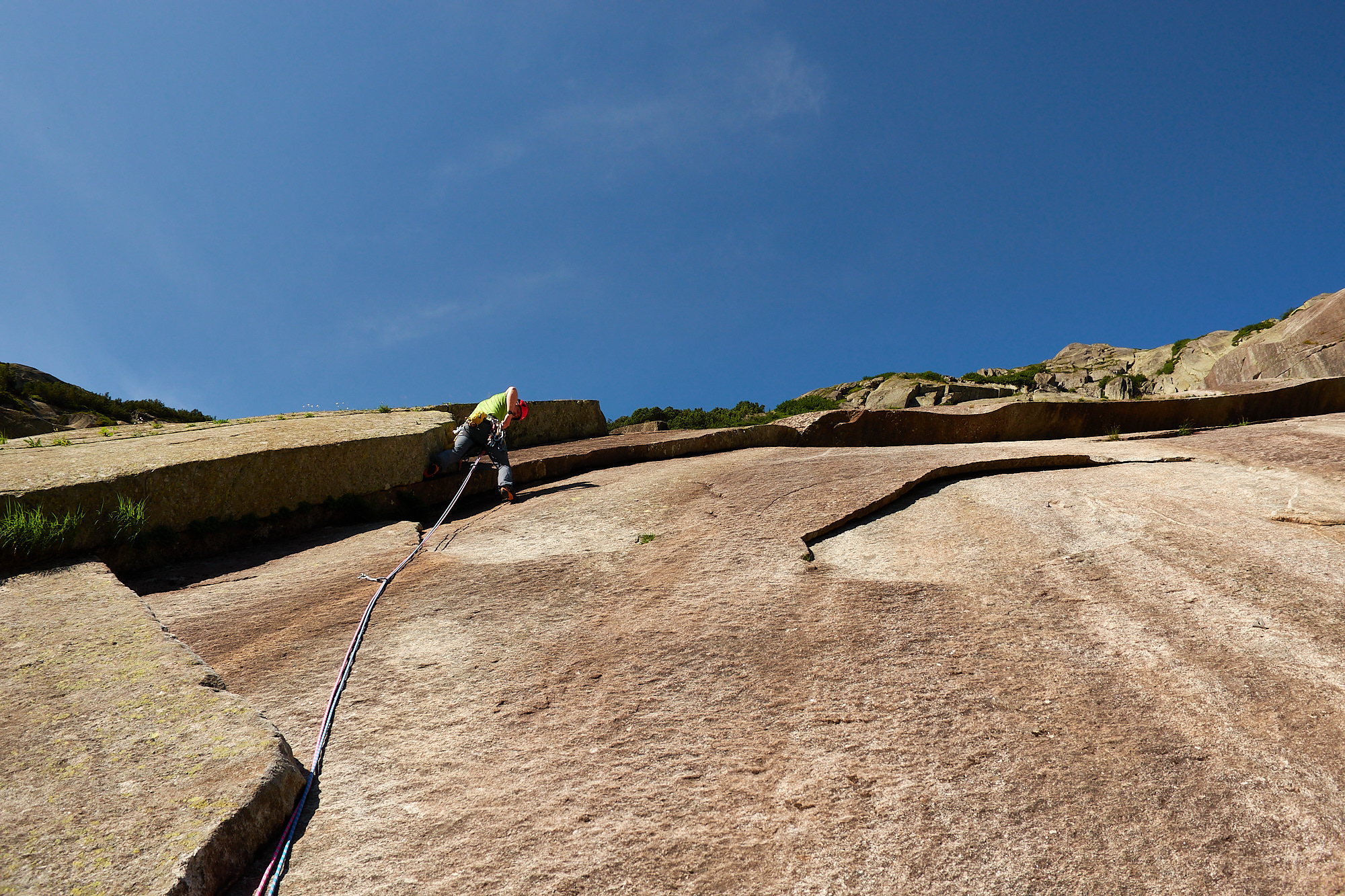 A climber in green in a corner on the left side of smooth brown and white granite slab with an overlap above