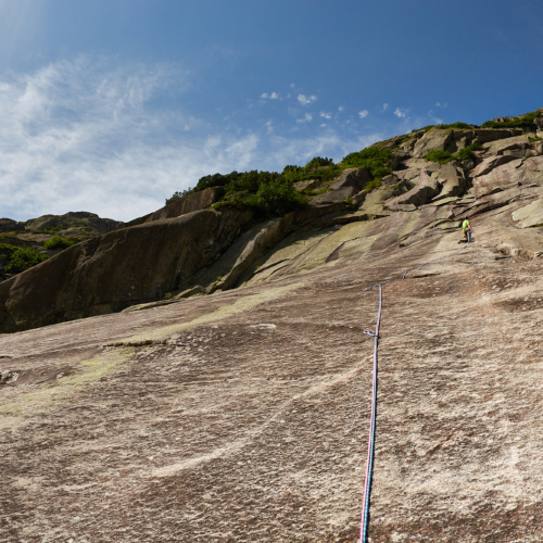 A climber in green in the middle of a smooth brown and white granite slab with overlaps above