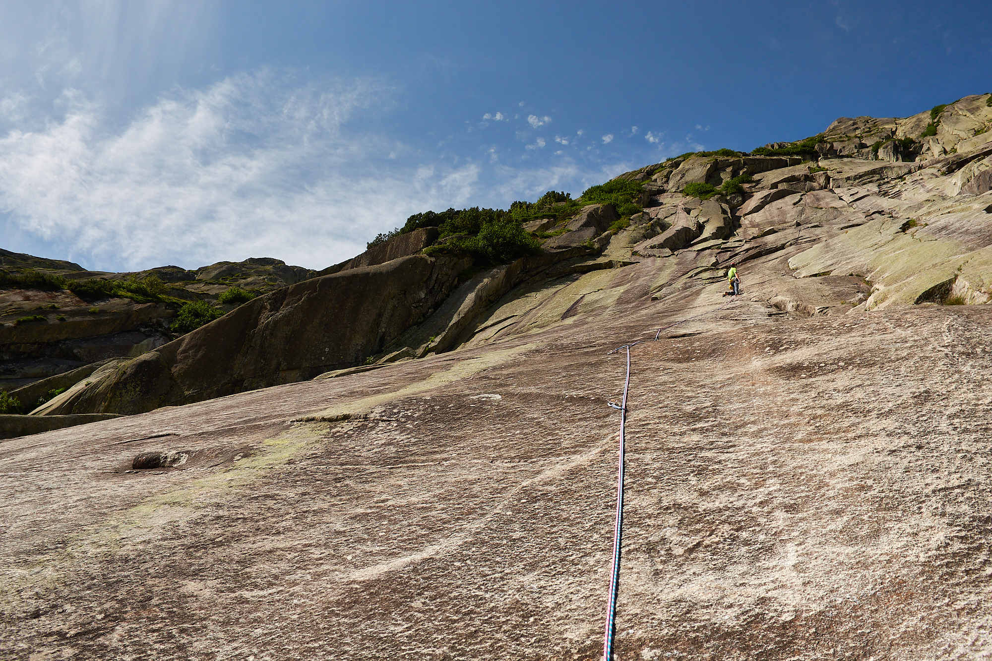 A climber in green in the middle of a smooth brown and white granite slab with overlaps above