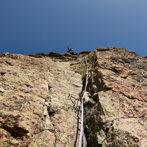 Looking up at a climber on a steep rock face with the ropes trailing down back towards the camera.