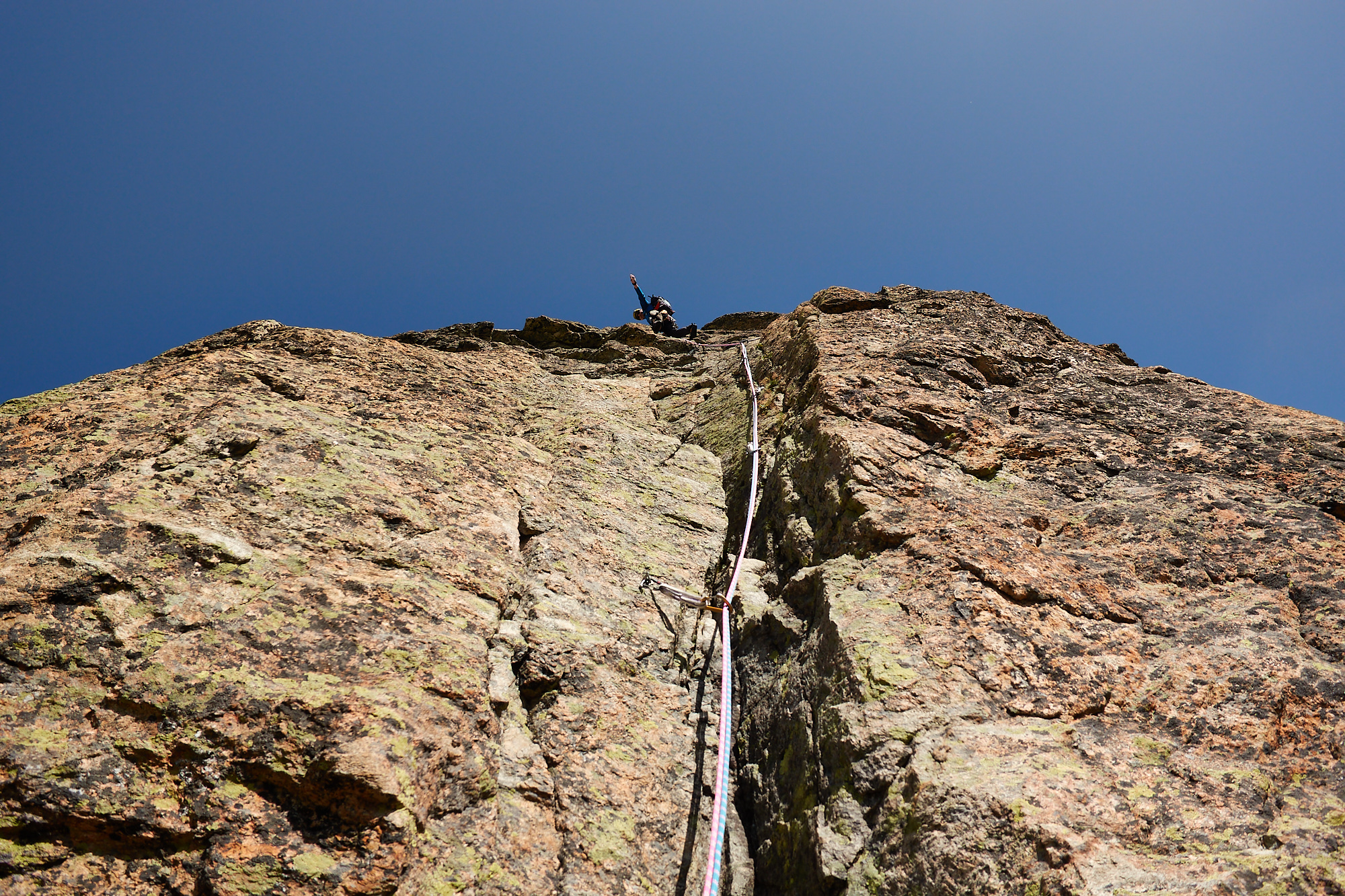 Looking up at a climber on a steep rock face with the ropes trailing down back towards the camera.