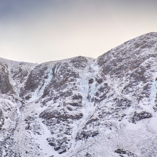 Looking up a broad gully on a mountain face in lean and icy winter condition. A number of blue icefalls line the walls of the gully.