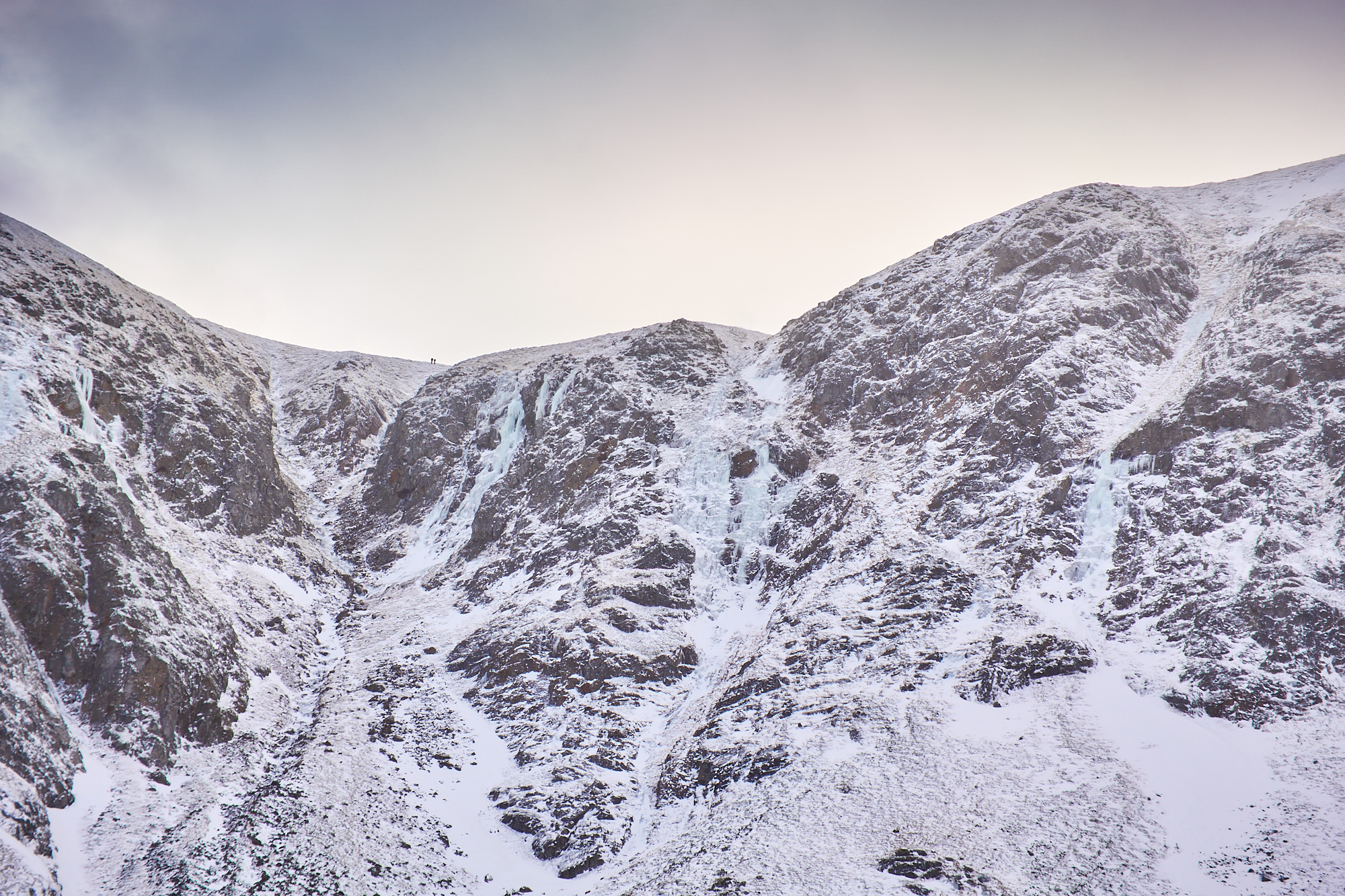 Looking up a broad gully on a mountain face in lean and icy winter condition. A number of blue icefalls line the walls of the gully.