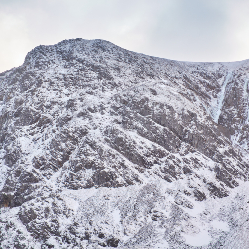 Looking up a narrow twisting on a mountain face in lean and icy winter condition. A number of blue icefalls line the walls of the gully.