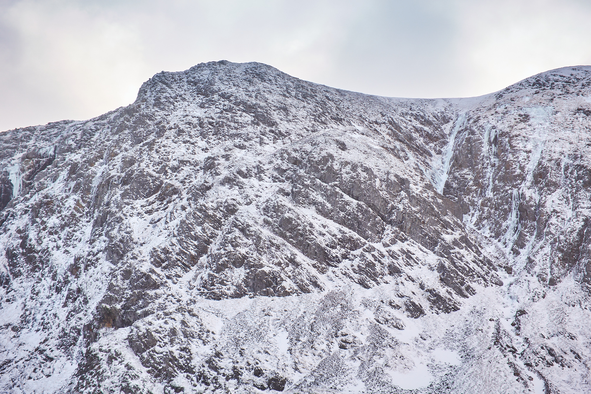 Looking up a narrow twisting on a mountain face in lean and icy winter condition. A number of blue icefalls line the walls of the gully.