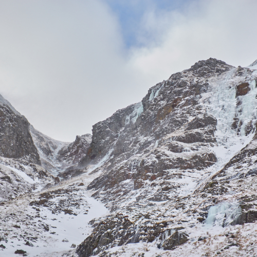 Looking up a broad gully on a mountain face in lean and icy winter condition. A number of blue icefalls line the walls of the gully.