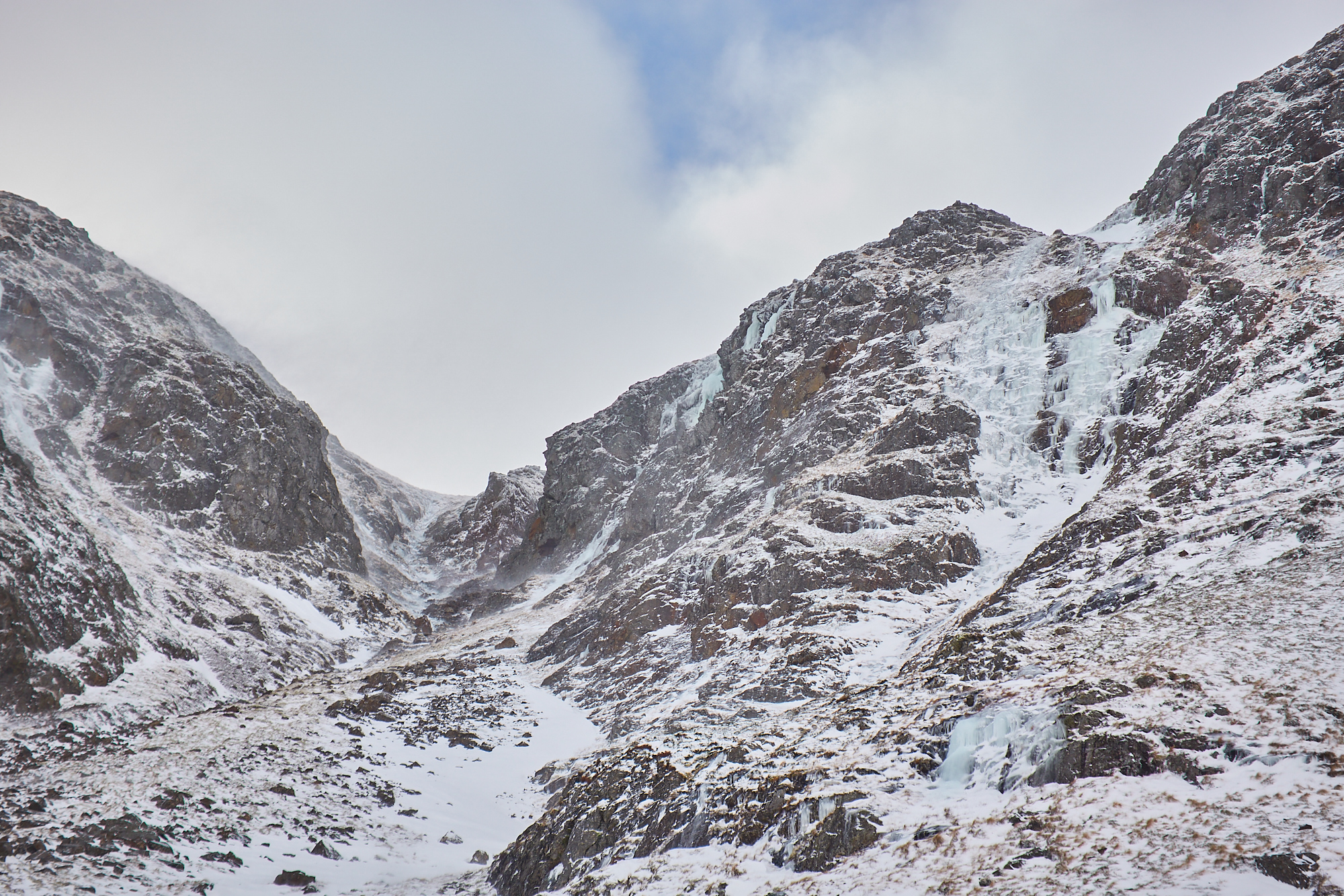 Looking up a broad gully on a mountain face in lean and icy winter condition. A number of blue icefalls line the walls of the gully.