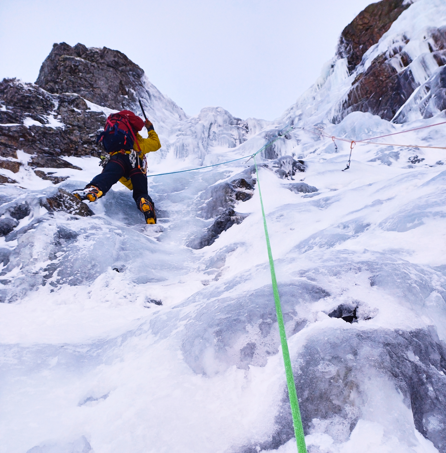 A climber in bright clothing swinging their ice axe as they climb a pitch of ice