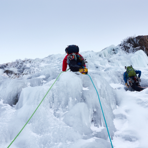 Two climbers in bright clothing swinging their ice axes as they climb a pitch of featured ice