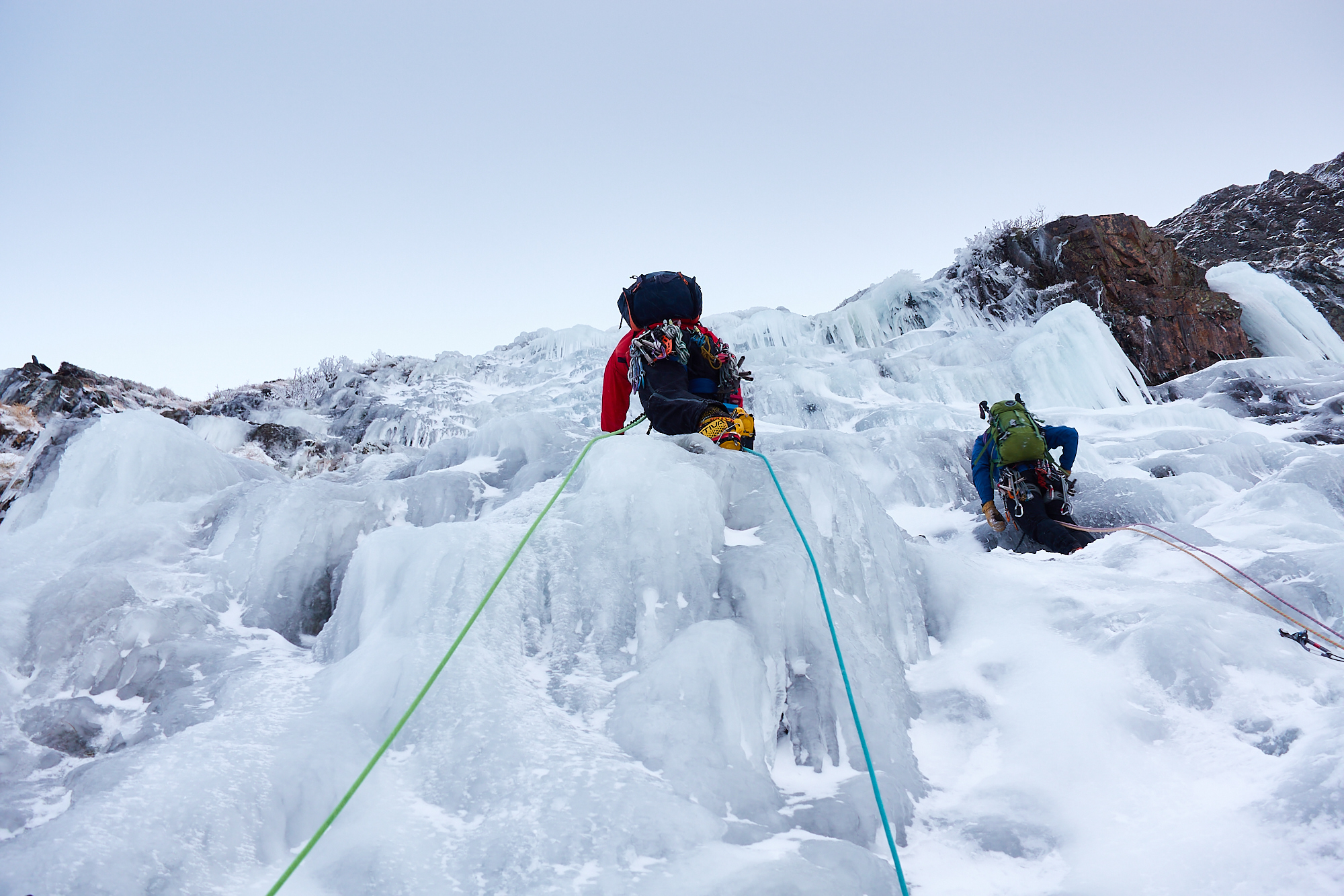 Two climbers in bright clothing swinging their ice axes as they climb a pitch of featured ice