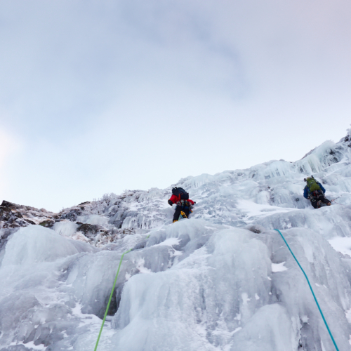 Two climbers in bright clothing swinging their ice axes as they climb a pitch of featured ice