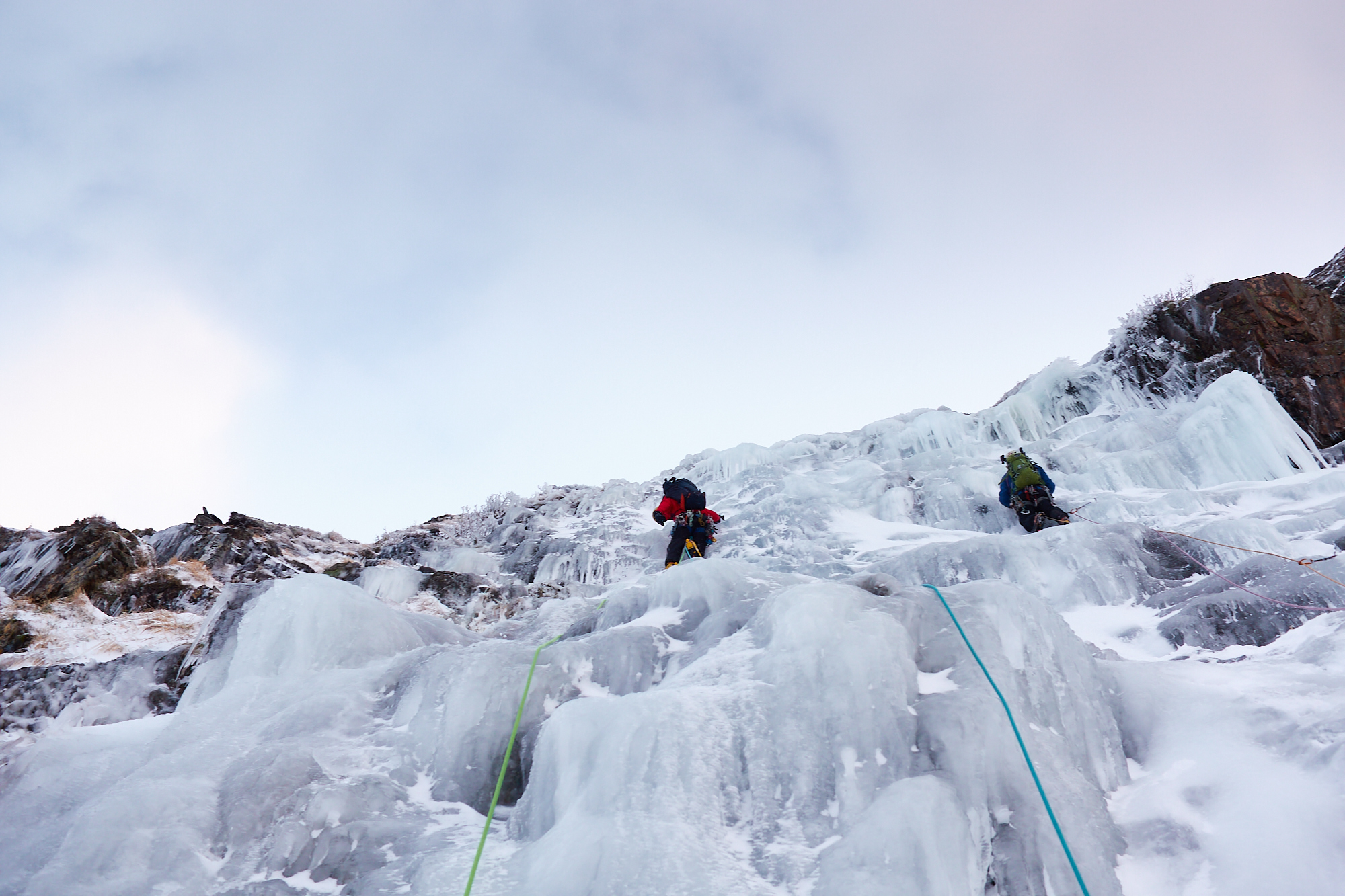 Two climbers in bright clothing swinging their ice axes as they climb a pitch of featured ice