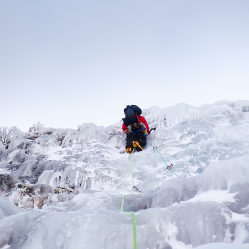 A climber in bright clothing swinging their ice axe as they climb a pitch of featured ice