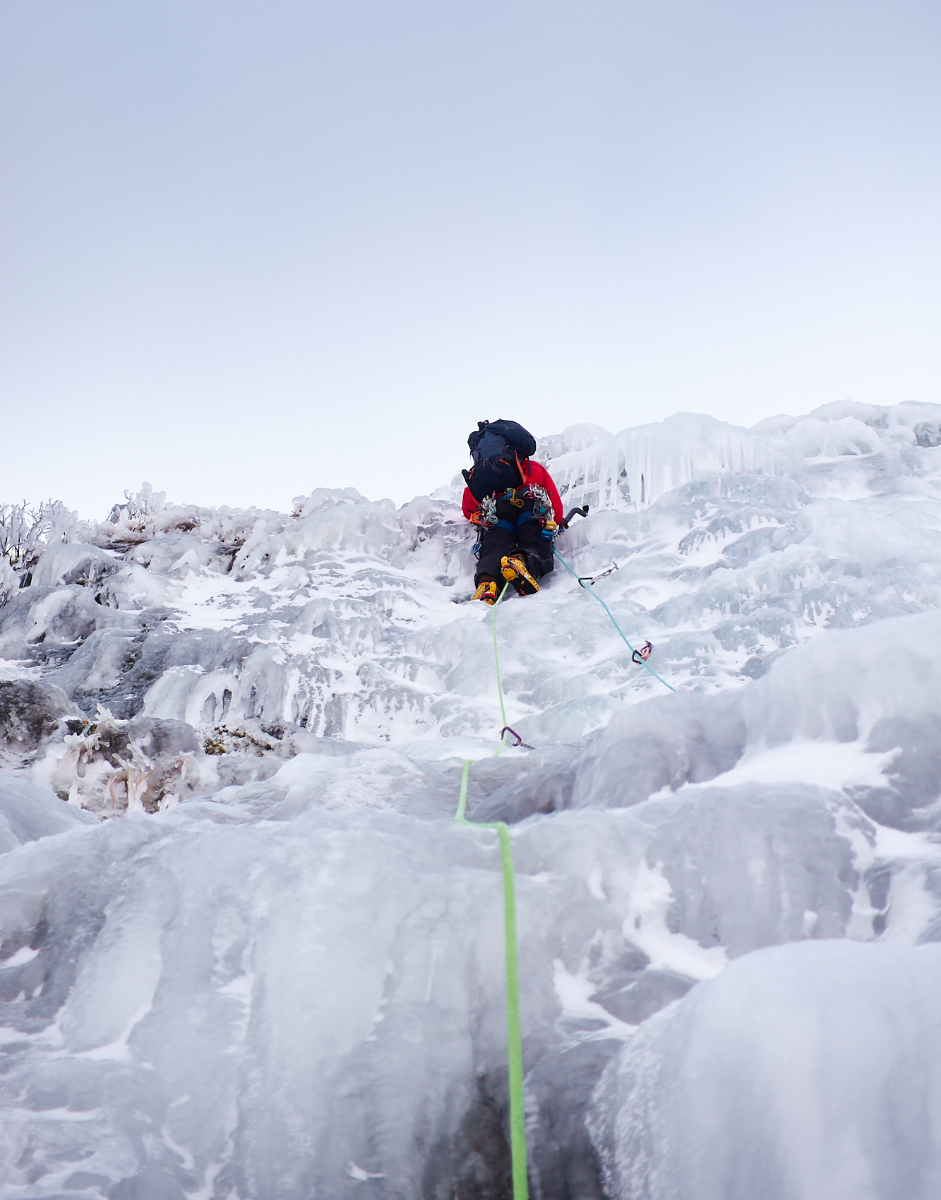 A climber in bright clothing swinging their ice axe as they climb a pitch of featured ice